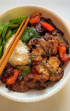 a bowl filled with meat and vegetables next to chopsticks on top of rice