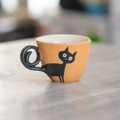 a coffee cup with a black cat painted on the side sitting on top of a table