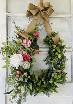 a wreath hanging on the front door with flowers and greenery around it's edges