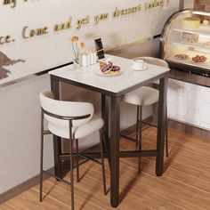 two white chairs sitting at a table in front of an open display case with pastries on it