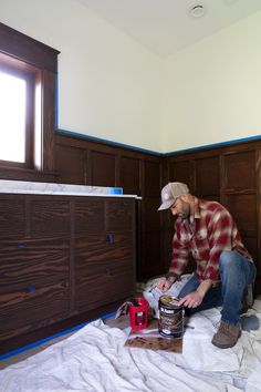 a man in plaid shirt and hat painting wooden furniture with blue tape on the floor