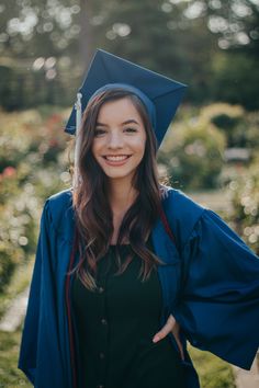 a woman wearing a blue graduation cap and gown posing for the camera with her hands on her hips