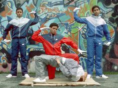 three men standing in front of a graffiti covered wall with one man on the ground