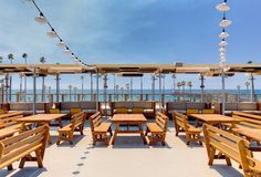 an outdoor dining area with wooden tables and umbrellas overlooking the ocean on a sunny day