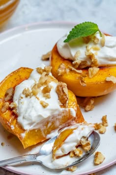 two pieces of peaches on a plate with whipped cream and walnuts next to them