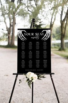 a black and white wedding seating sign with flowers on it in front of some trees