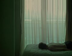 a naked man laying on top of a bed in front of a curtained window