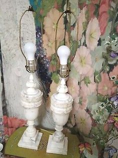 two white lamps sitting on top of a green table next to a wallpapered background