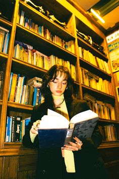 a woman reading a book in front of a bookshelf