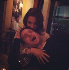 a man and woman hugging each other at a table with wine glasses in front of them