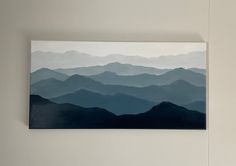 a painting hanging on the wall with mountains in the background