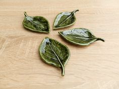 three green leaf shaped dishes sitting on top of a wooden table