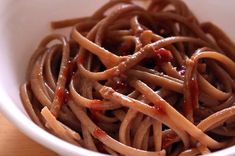 a white bowl filled with pasta covered in bbq sauce on top of a wooden table