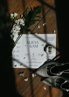 a pair of black shoes sitting on top of a wooden floor next to a bouquet of flowers