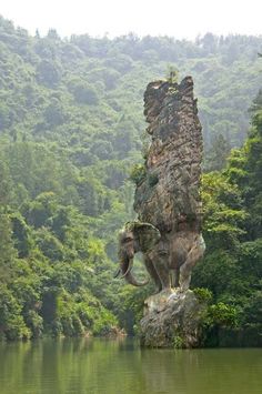 an elephant statue on top of a rock in the middle of a lake surrounded by trees