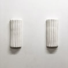 two white vases sitting next to each other on top of a table in front of a wall