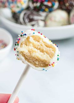 a hand holding a cake pops with white frosting and sprinkles