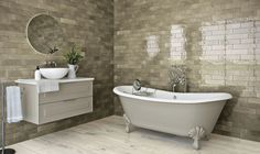 a white bath tub sitting next to a sink under a bathroom mirror on a wooden floor