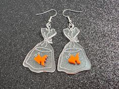 two fish in a bag shaped earrings on a black surface with silver earwires