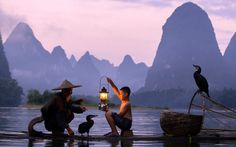 three people sitting on a raft in the water, one holding a lantern while the other holds a bird