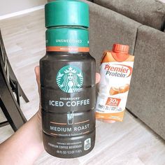 a person holding up a bottle of iced coffee next to a couch with two bags of coffee on it