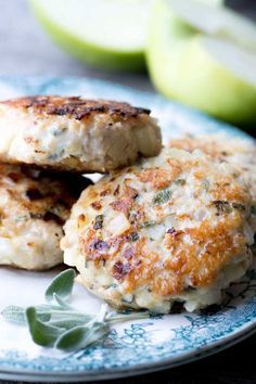 two crab cakes on a plate with apples in the background