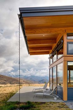 a wooden house with two lawn chairs on the front porch and an open patio area