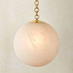 a white ball hanging from a gold chain on a light colored wallpapered background