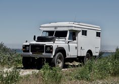 an old white truck parked on the side of a road next to grass and bushes