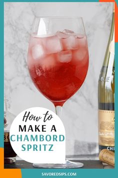 a wine glass filled with red liquid and ice cubes next to a bottle of champagne