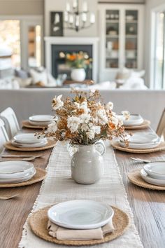 a dining room table with place settings and flowers in a vase on the centerpiece