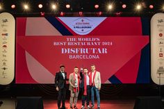 three men standing on stage in front of a large screen with the world's best restaurant