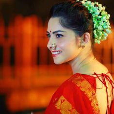 a woman in a red dress with green flowers on her head smiling at the camera