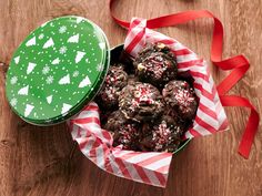 a green tin filled with chocolate covered cookies on top of a wooden table next to a red and white ribbon