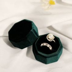 an open ring box sitting on top of a white bed next to a single flower