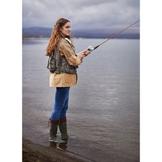 a woman is standing on the shore with her fishing rod