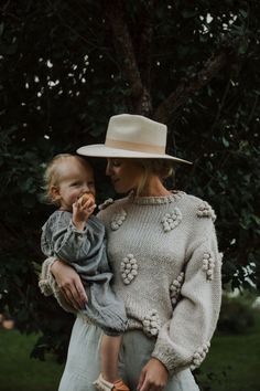 a woman holding a baby while wearing a hat