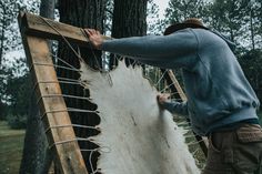 a man holding onto a piece of wood that is being nailed to a tree trunk