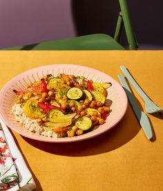 a pink plate topped with vegetables and rice next to silverware on a yellow table