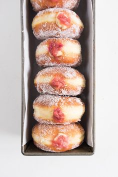 four donuts in a box with powdered sugar and strawberry toppings on them