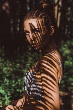 a woman sitting in the woods with her shadow cast on her chest and arm behind her back