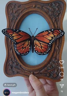 a hand holding up a wooden frame with a butterfly on it