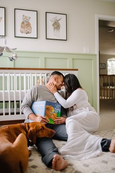 a man and woman sitting on the floor next to a dog with a book in their lap