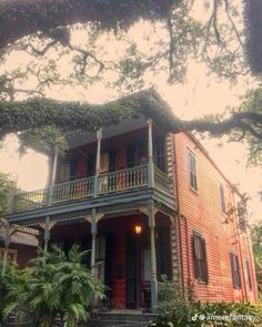 an old red house with porches and balconies on the second floor is surrounded by trees