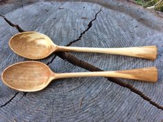 two wooden spoons sitting on top of a tree stump next to eachother