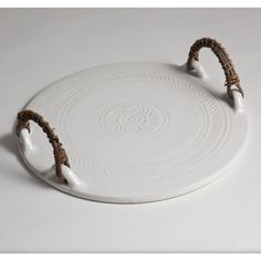 a white platter with two brown handles and rope around the rim, on a white surface