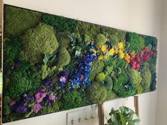 a living wall with flowers and plants on it's side is displayed in a room