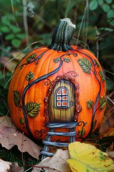 an orange pumpkin with a house painted on it sitting in the grass next to leaves