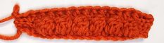 an orange crochet stitch on top of a white surface with one end missing