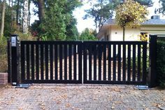 a black gate in front of a house with leaves on the ground and trees behind it